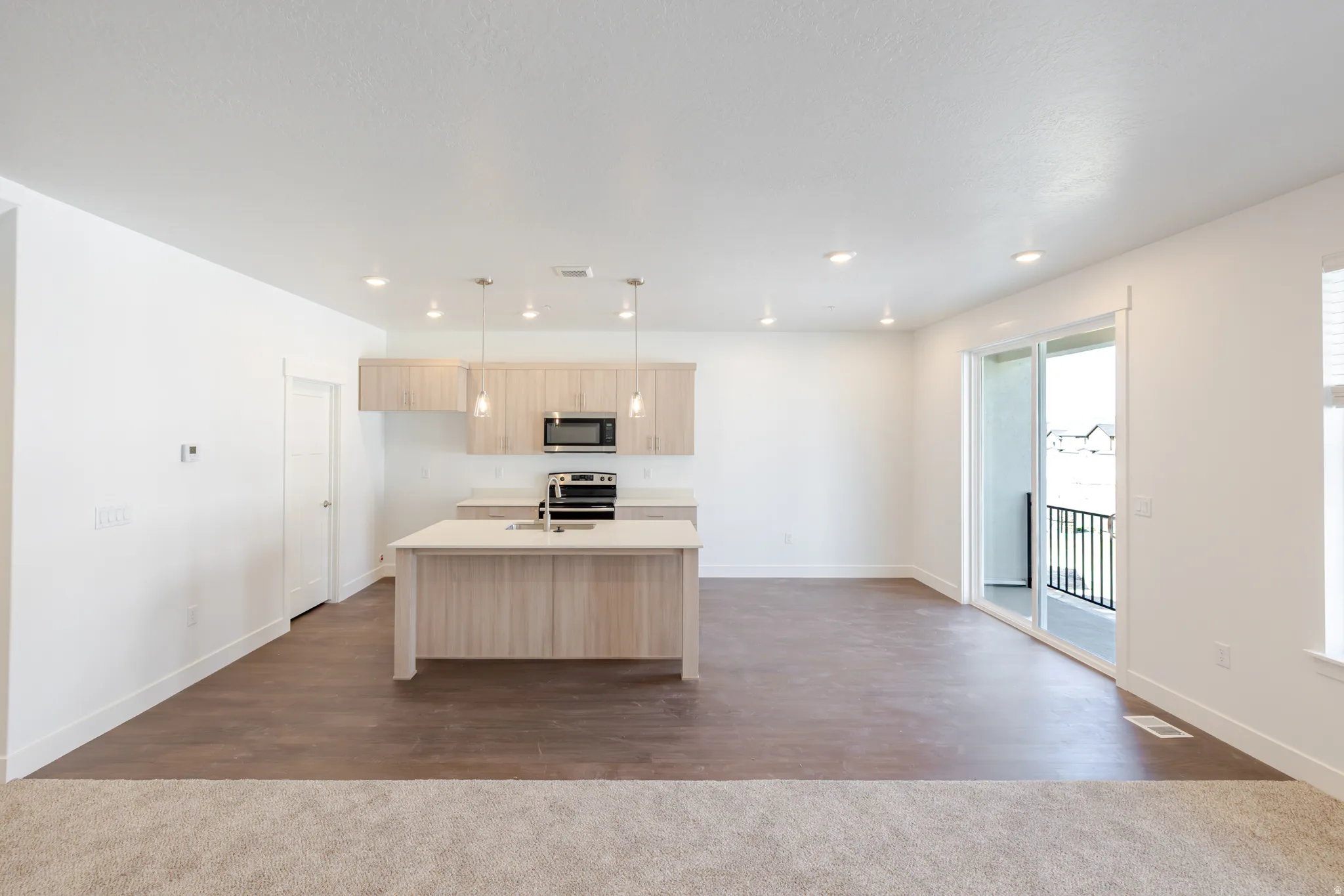 Kitchen with light wood finish cabinetry, a kitchen island with sink, stainless steel appliances, pendant lighting, and dark wood-style floors