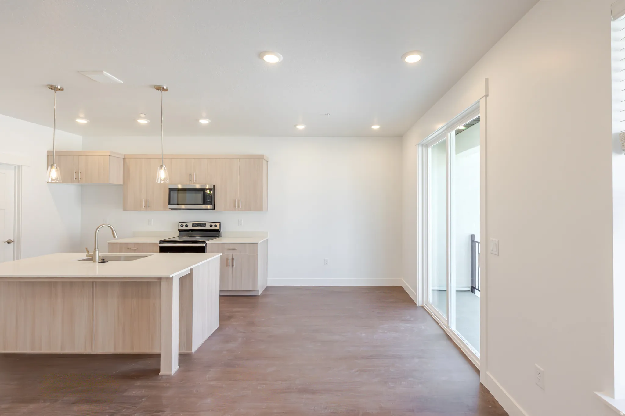 Kitchen with light wood finish cabinetry, hanging light fixtures, a center island with sink, stainless steel appliances, and dark wood-type flooring