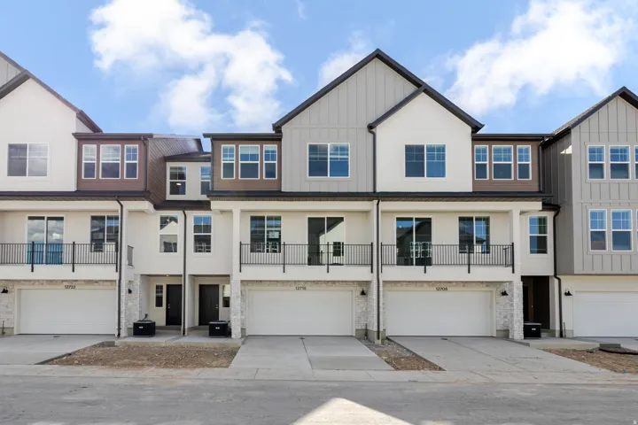 View of front of property featuring a balcony, a garage, driveway, board and batten siding, and stucco siding