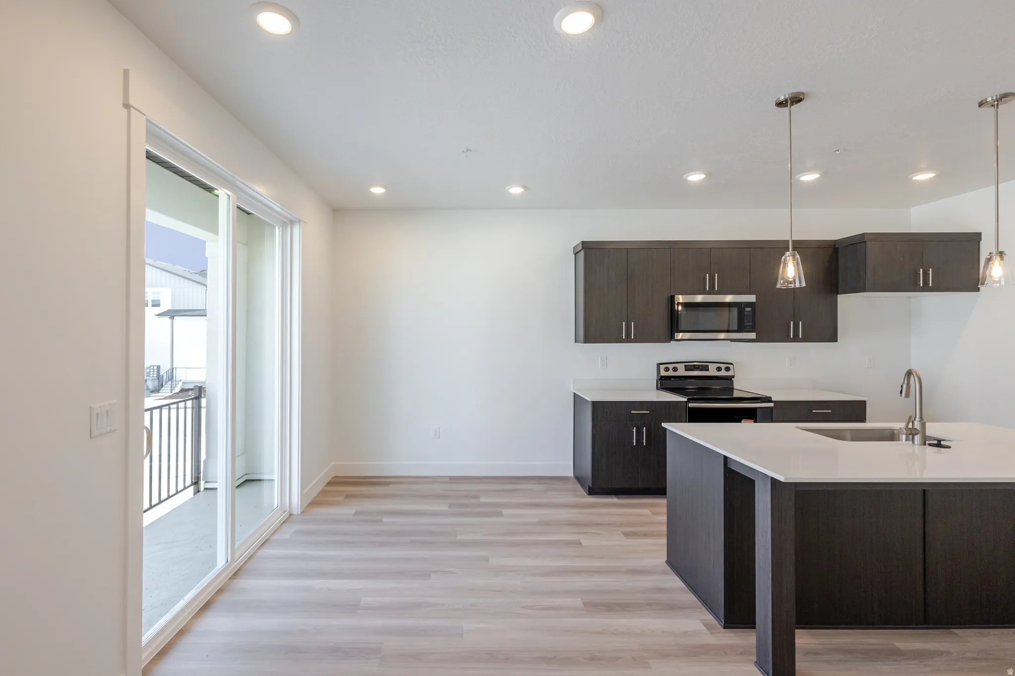 Kitchen featuring dark wood finish cabinetry, decorative light fixtures, stainless steel appliances, light wood-style floors, and light stone counters