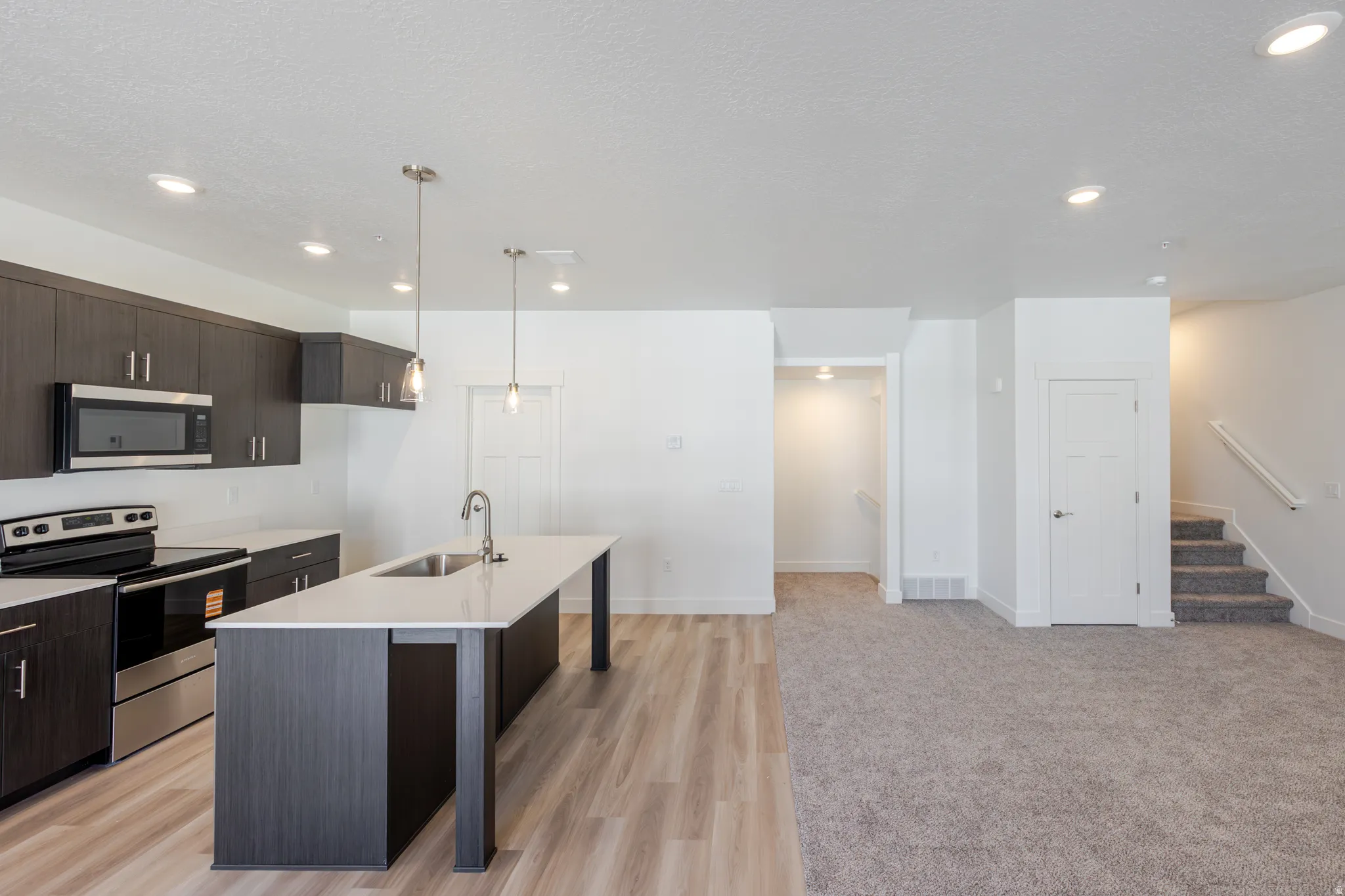 Kitchen with dark wood finish cabinetry, stainless steel appliances, a kitchen island with sink, a breakfast bar, and pendant lighting