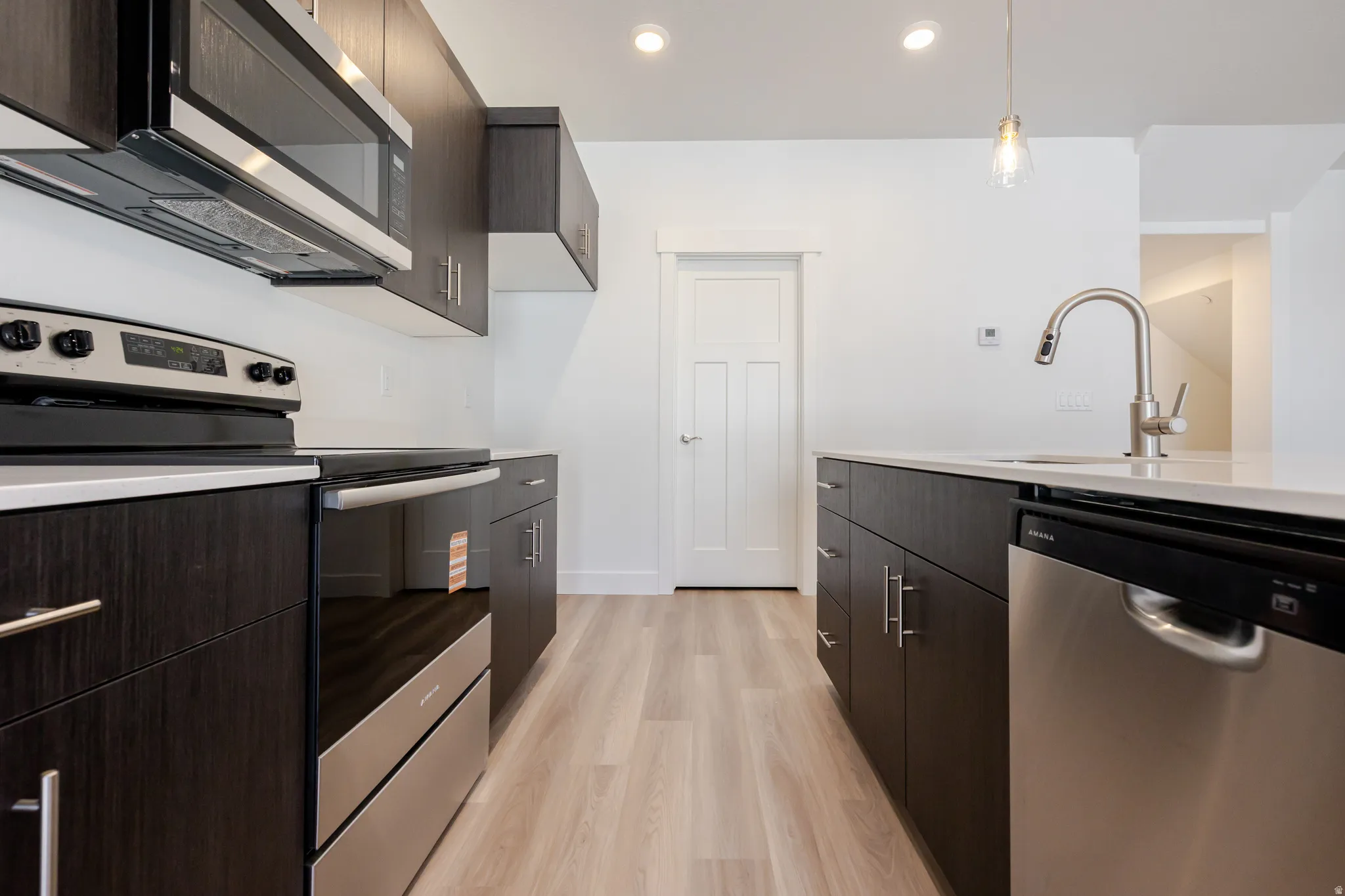 Kitchen featuring stainless steel appliances, light wood finished floors, dark wood finish cabinetry, modern cabinets, and light stone counters