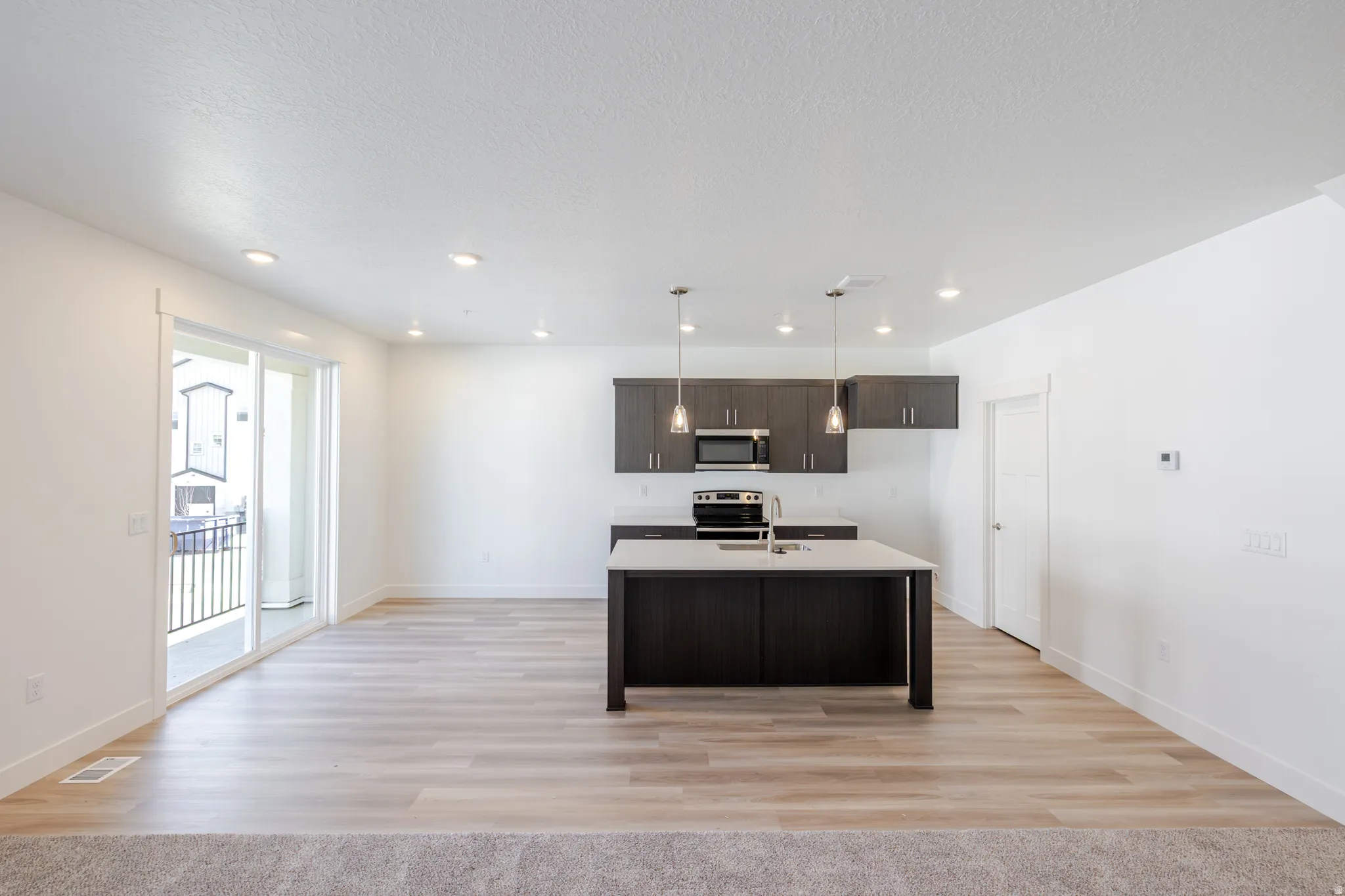 Kitchen featuring dark wood finish cabinetry, light wood-style floors, a kitchen island with sink, pendant lighting, and stainless steel appliances