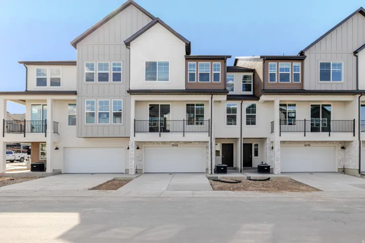 View of front of home with a balcony, board and batten siding, an attached garage, concrete driveway, and stucco siding
