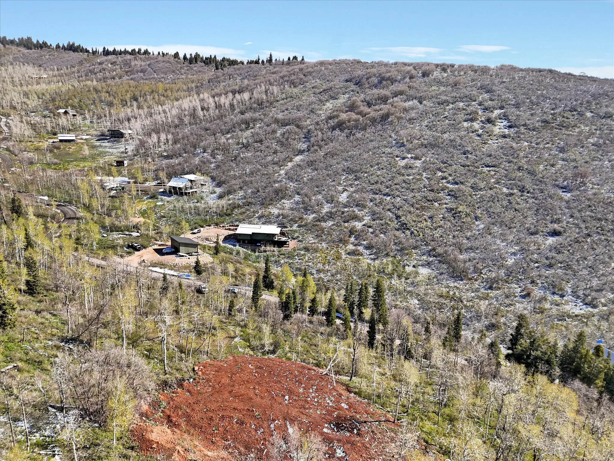 Expansive mountain landscape featuring varied topography, mature deciduous and evergreen trees, and a distant residential structure