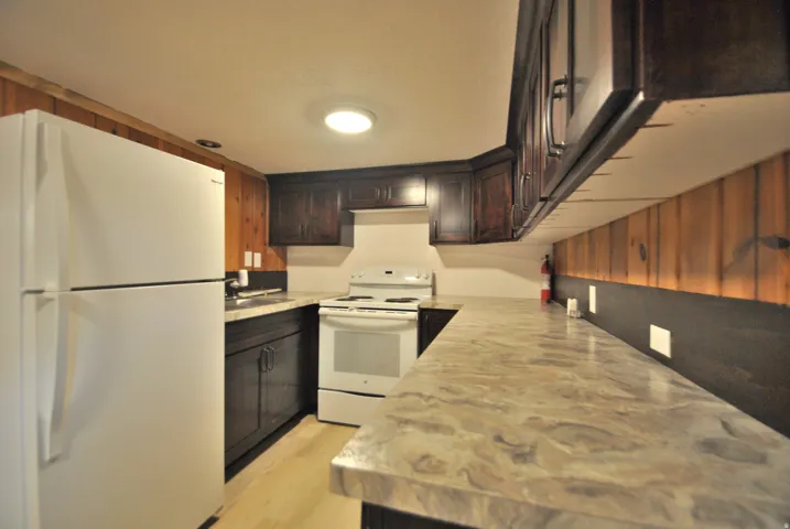 Kitchen featuring white appliances, light wood finished floors, and dark brown cabinetry