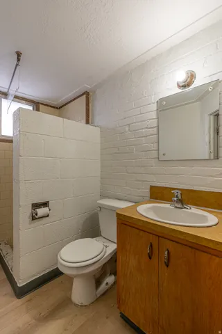 Full bathroom featuring vanity, light wood-type flooring, concrete block wall, a textured ceiling, and a walk in shower
