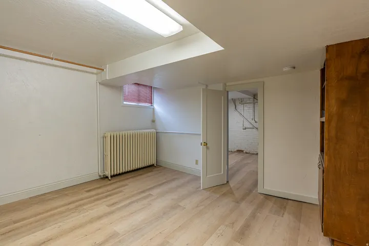 Finished below grade area with radiator, light wood-style floors, and brick wall