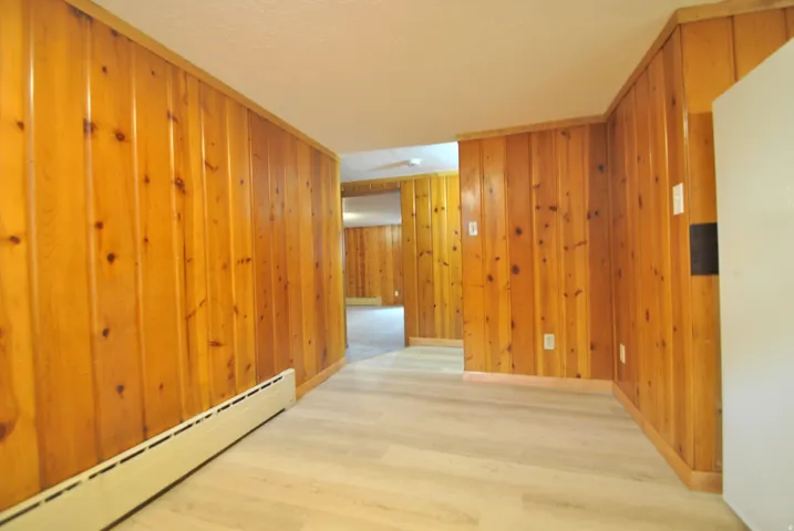 Hall featuring a baseboard heating unit, wood finished floors, and wooden walls
