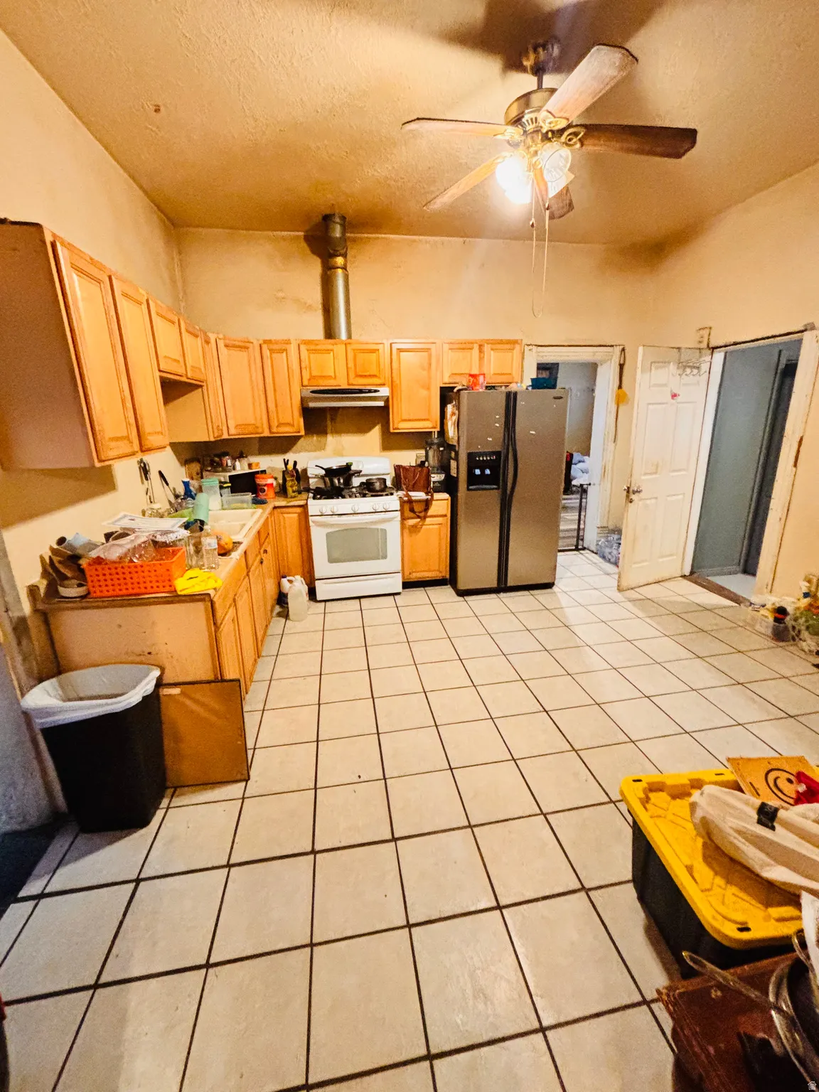 Kitchen with light wood-finish cabinetry, white tile flooring, and a ceiling fan
