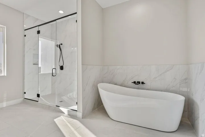 Bathroom with a freestanding tub, a marble finish shower, tile walls, recessed lighting, and a wainscoted wall