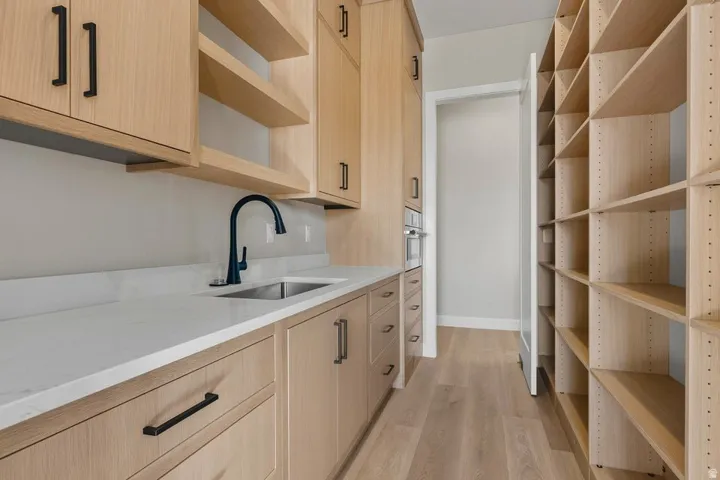 Kitchen featuring light brown cabinetry, open shelves, light wood-style flooring, light stone countertops, and oven