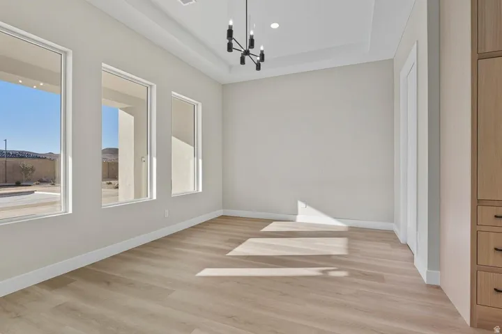 Empty room with a chandelier, light wood-style flooring, a raised ceiling, healthy amount of natural light, and recessed lighting