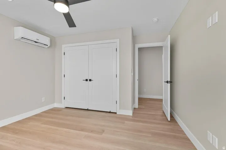Unfurnished bedroom featuring a wall mounted air conditioner, light wood finished floors, a closet, and ceiling fan