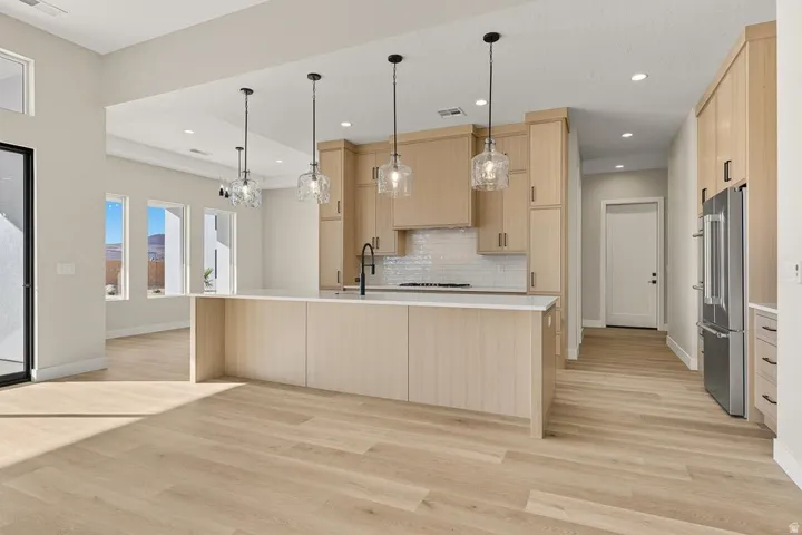 Kitchen featuring light brown cabinets, pendant lighting, high end fridge, backsplash, and light wood-type flooring