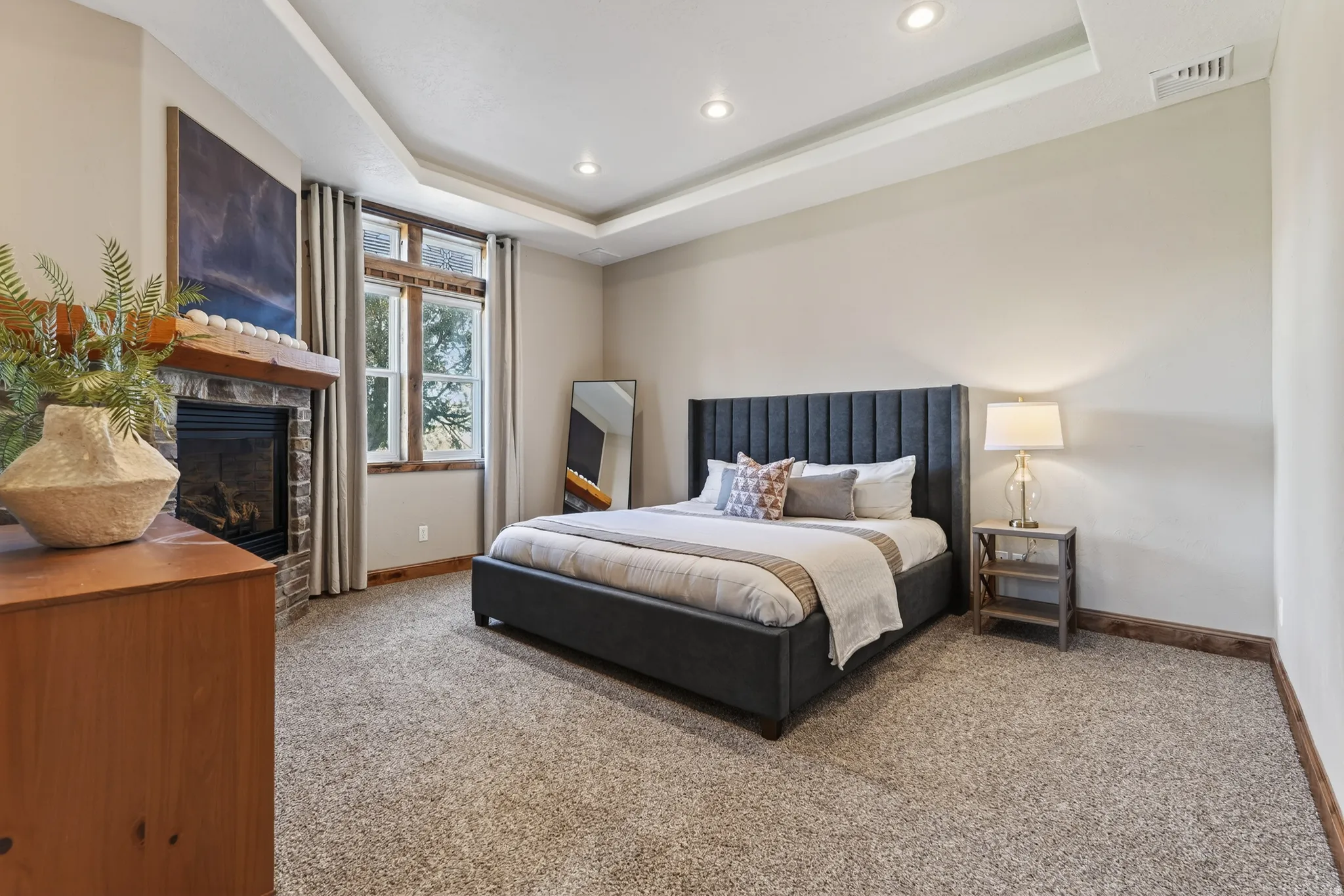 Bedroom with carpet, a glass covered fireplace, a tray ceiling, and recessed lighting