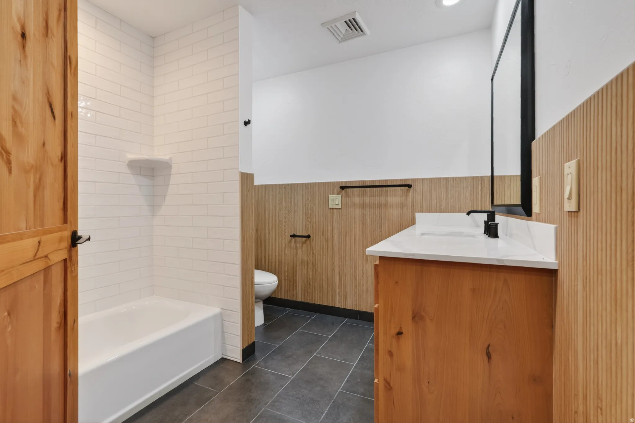 Bathroom with vanity, tub / shower combination, wainscoting, dark tile patterned flooring, and wooden walls