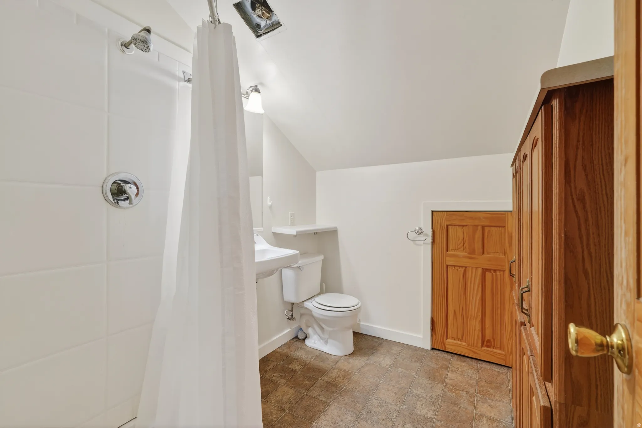 Bathroom with lofted ceiling, a shower with curtain, and stone finish floors