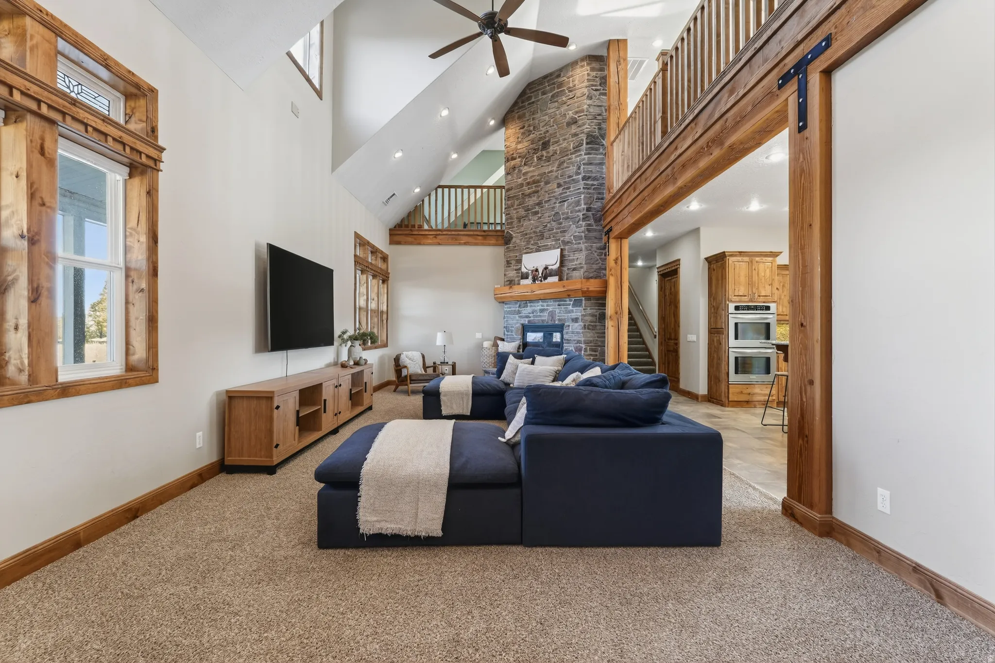Living room featuring ceiling fan, a large fireplace, a high ceiling, stairs, and light carpet