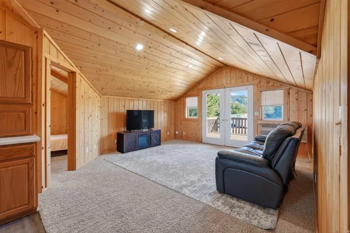 Living area with wooden walls, wooden ceiling, french doors, vaulted ceiling, and carpet flooring