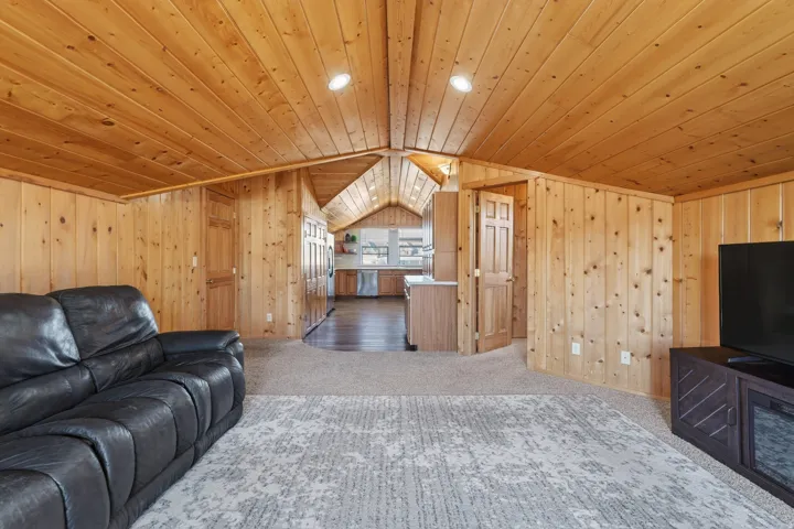 Carpeted living room featuring lofted ceiling, wooden ceiling, and wooden walls