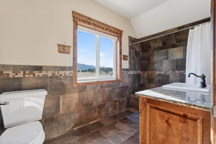 Bathroom featuring tile walls, a tile shower, a wainscoted wall, and vanity
