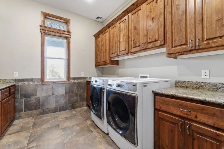 Washroom featuring cabinet space, washing machine and dryer, wainscoting, and stone finish floors