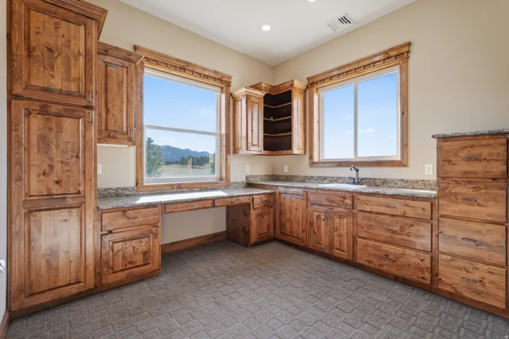 Kitchen featuring built in desk, open shelves, light stone countertops, and brown cabinets