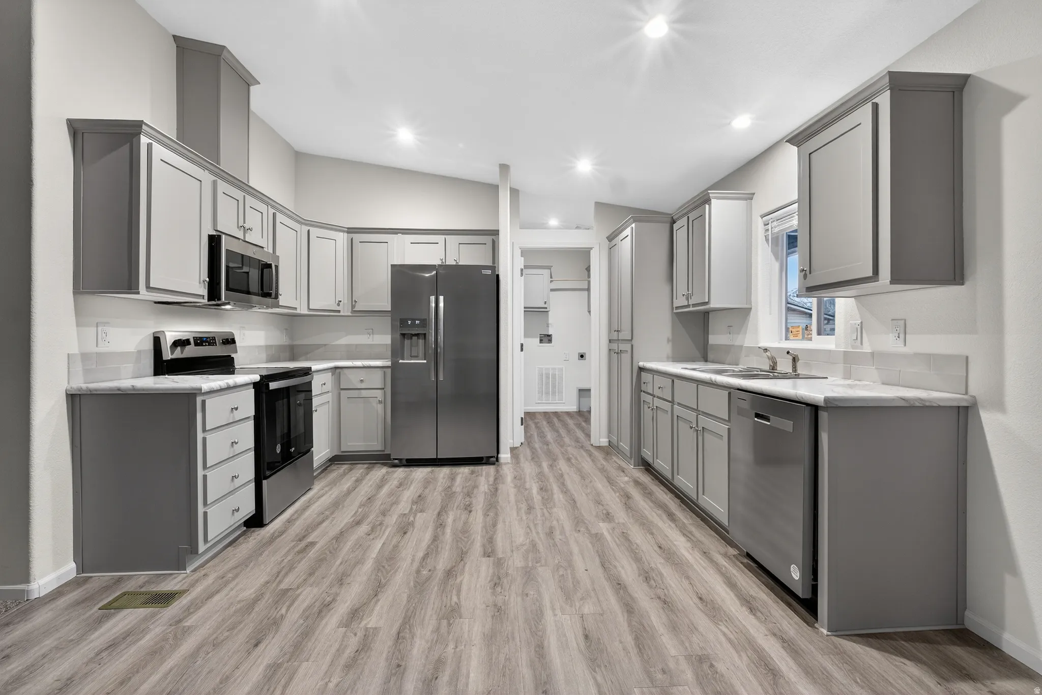 Kitchen featuring gray cabinetry, appliances with stainless steel finishes, lofted ceiling, light wood-style flooring, and recessed lighting