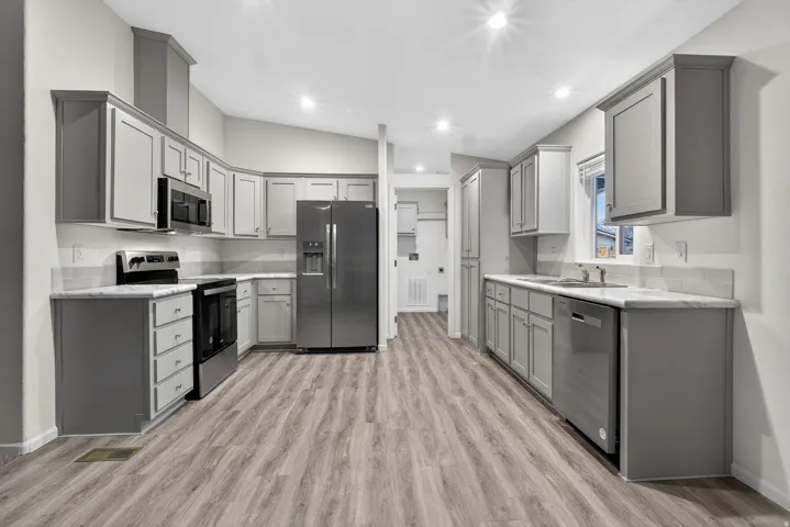 Kitchen featuring gray cabinetry, appliances with stainless steel finishes, lofted ceiling, light wood-style flooring, and recessed lighting