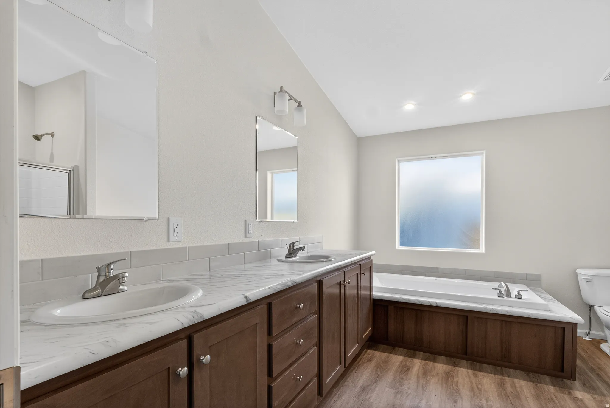 Full bathroom featuring double vanity, a garden tub, and light wood finished floors