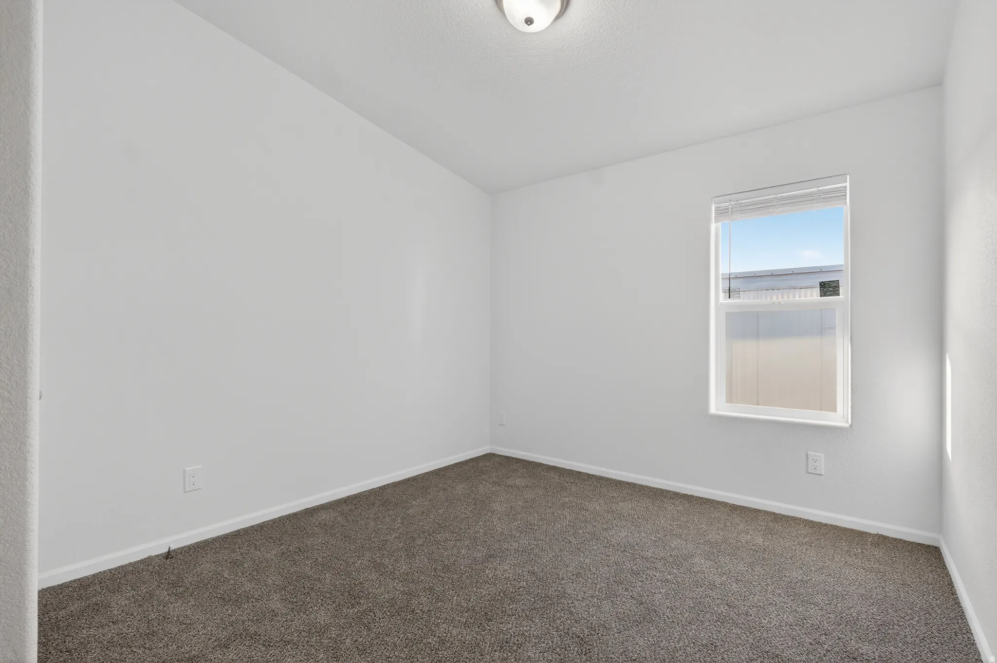 Carpeted empty room featuring baseboards and lofted ceiling