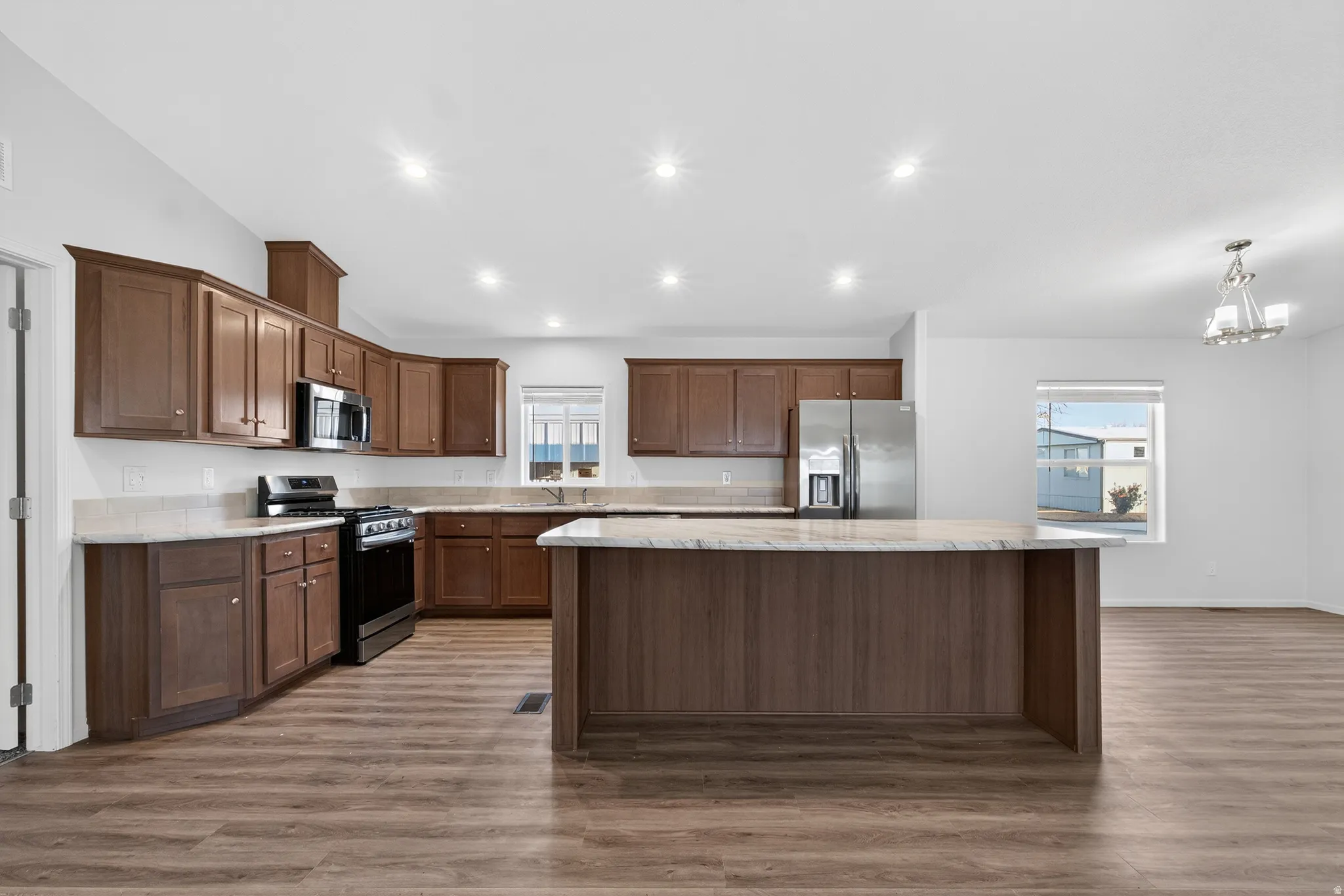 Kitchen featuring appliances with stainless steel finishes, vaulted ceiling, light wood-style flooring, healthy amount of natural light, and a center island
