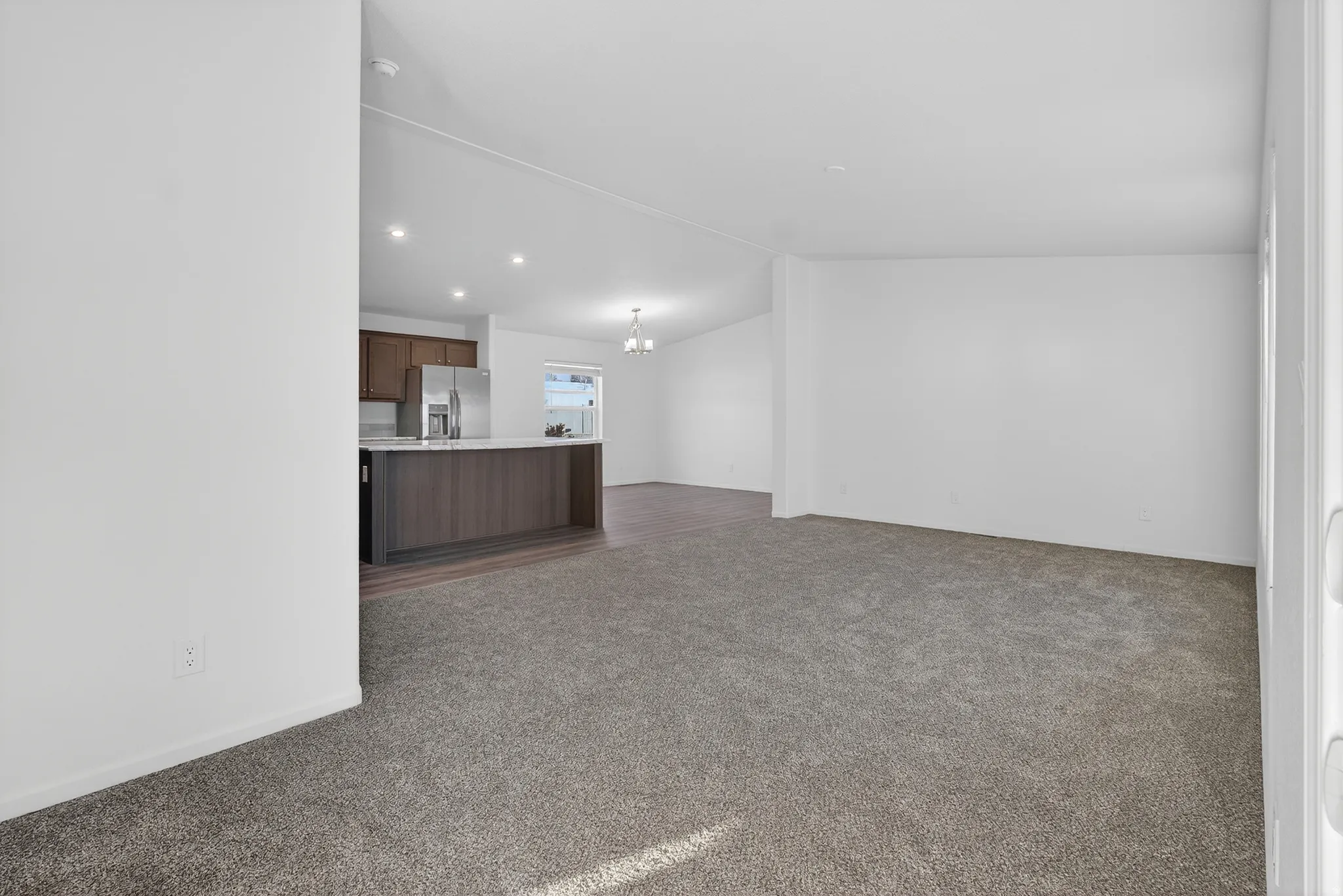 Unfurnished living room with dark carpet, vaulted ceiling, a chandelier, and recessed lighting