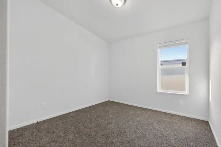 Carpeted empty room featuring baseboards and lofted ceiling