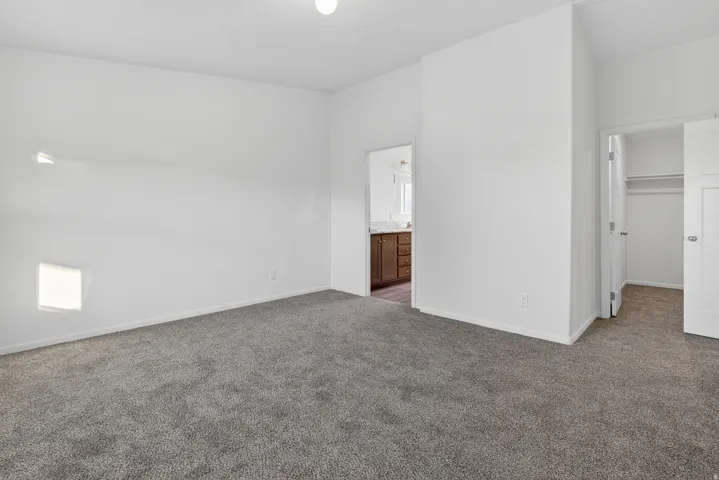 Unfurnished bedroom featuring a spacious closet, dark colored carpet, and ensuite bath