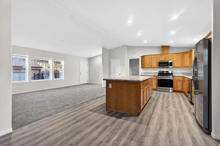 Kitchen with vaulted ceiling, stainless steel appliances, open floor plan, a center island, and light stone counters