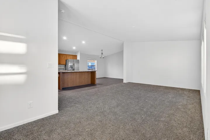 Unfurnished living room featuring vaulted ceiling, dark colored carpet, and recessed lighting