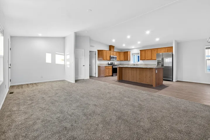 Kitchen with open floor plan, light carpet, brown cabinetry, appliances with stainless steel finishes, and lofted ceiling