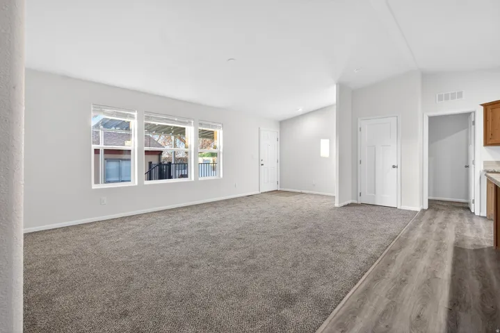 Unfurnished living room featuring vaulted ceiling, dark colored carpet, and dark wood-style flooring