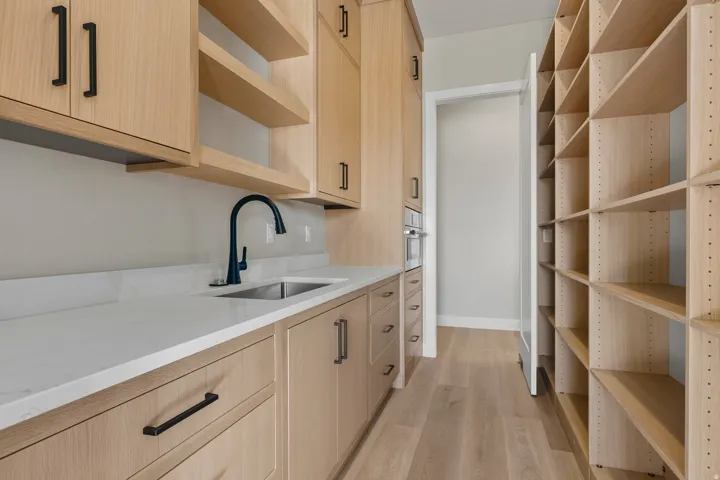 Kitchen with light brown cabinets, open shelves, light wood-style floors, light stone countertops, and stainless steel oven