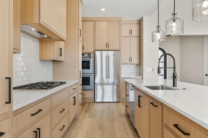 Kitchen featuring light brown cabinets, appliances with stainless steel finishes, pendant lighting, light wood-style flooring, and light stone counters