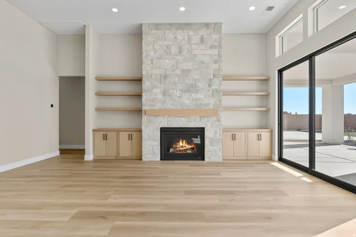 Unfurnished living room with a stone fireplace, recessed lighting, built in features, light wood finished floors, and a high ceiling