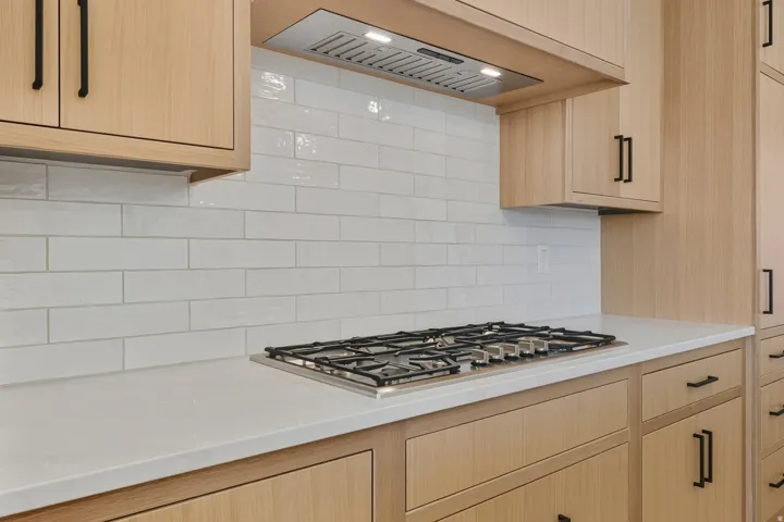 Kitchen featuring custom exhaust hood, light brown cabinets, stainless steel gas cooktop, light stone countertops, and tasteful backsplash