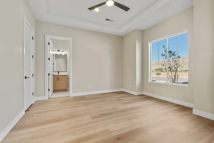 Unfurnished bedroom with light wood finished floors, a tray ceiling, a ceiling fan, recessed lighting, and connected bathroom