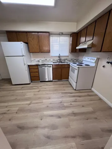 Kitchen featuring white appliances, light countertops, light wood finished floors, under cabinet range hood, and brown cabinetry