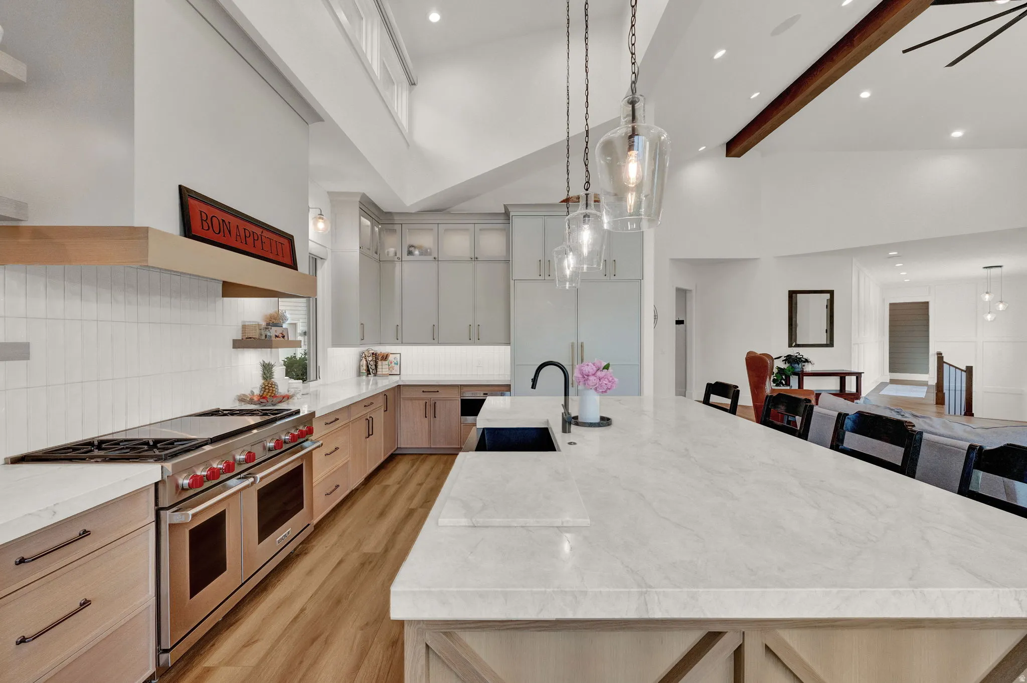 Kitchen featuring a large island, range with two ovens, pendant lighting, light stone countertops, and high vaulted ceiling
