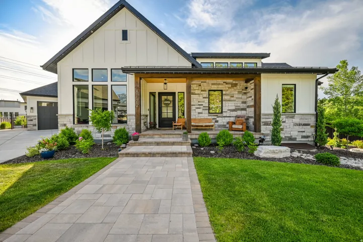 View of front of property featuring board and batten siding, stone siding, a front yard, covered porch, and a standing seam roof