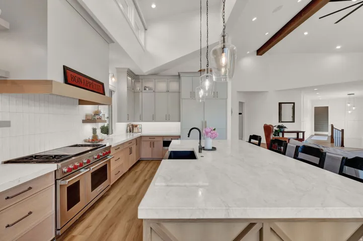 Kitchen featuring a large island, range with two ovens, pendant lighting, light stone countertops, and high vaulted ceiling