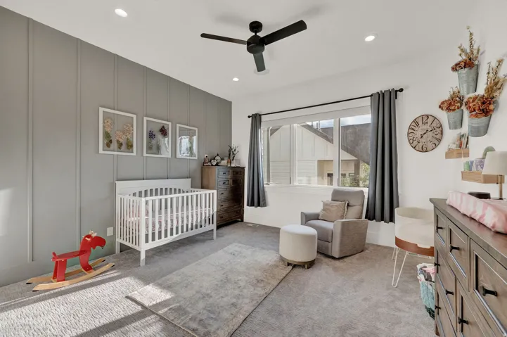 Bedroom with a decorative wall, a nursery area, light colored carpet, ceiling fan, and an accent wall
